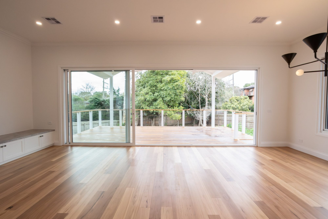 Open living room with a white aluminium stacking door opening onto the rear deck, Ringwood North